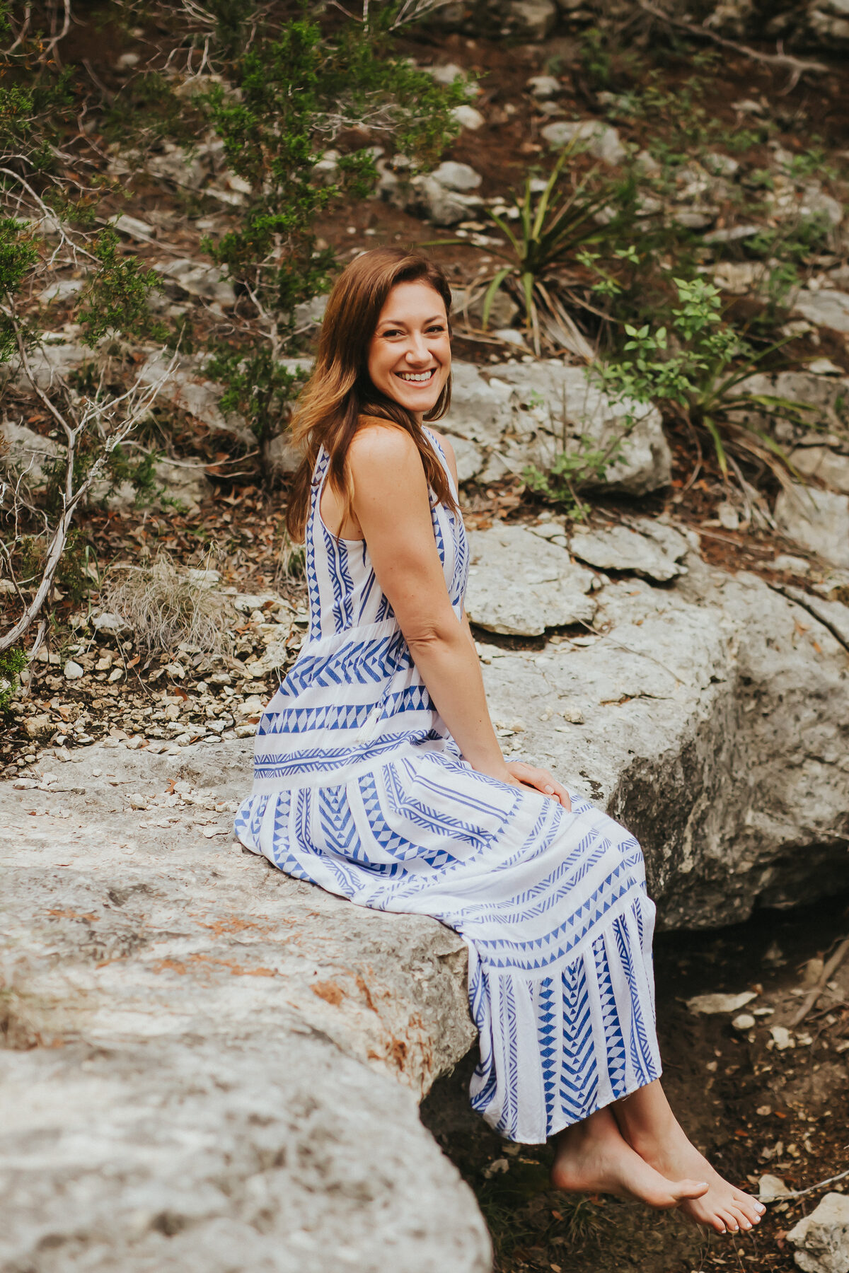 Amanda Moody smiling, seated on limestone rocks in a blue and white dress
